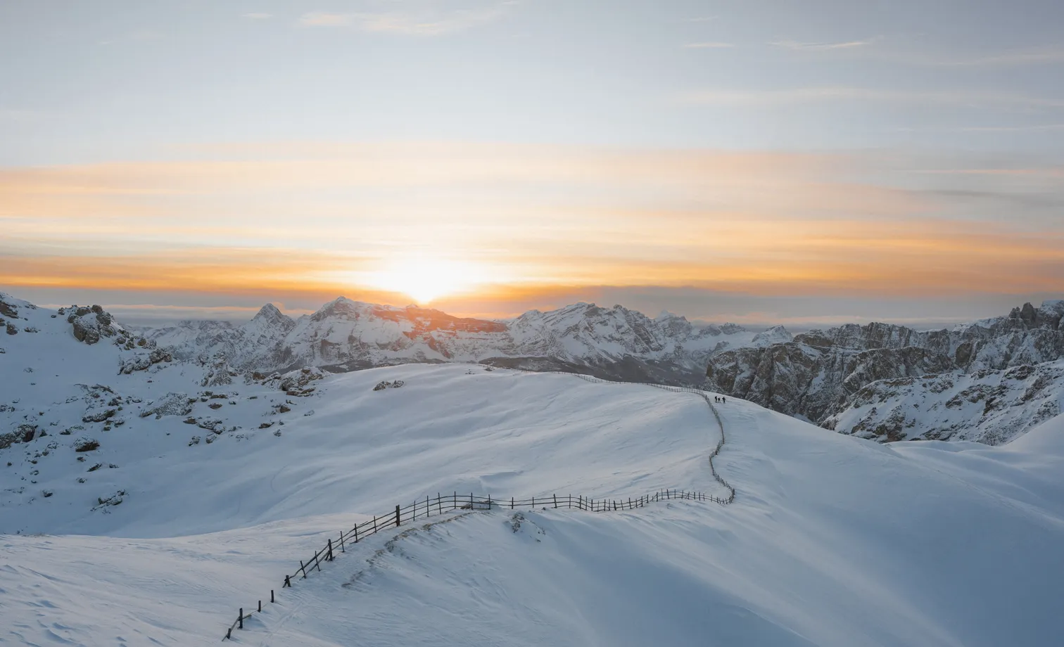 Snow-covered high plateau with wooden fence at sunset over the Geisler Dolomites, hiker on winter trail near Villnöß