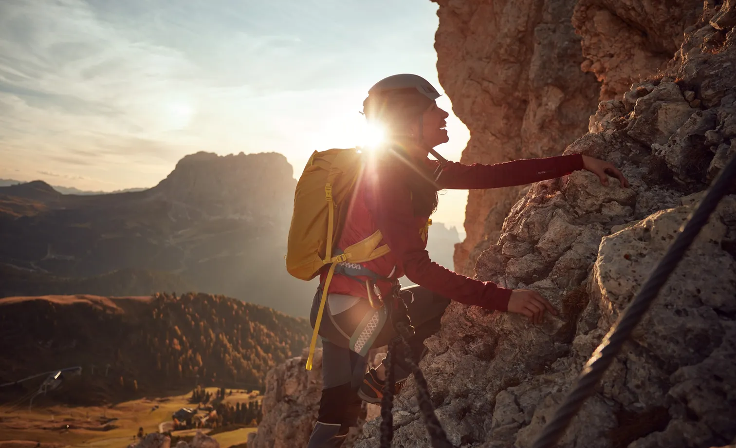 Female climber on the via ferrata of the Geisler group at sunrise with Dolomite panorama and golden larches