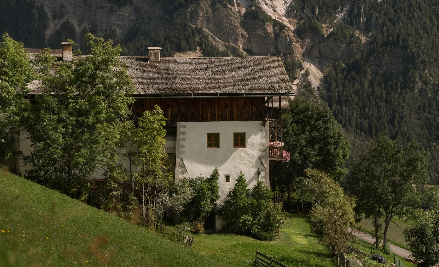 Traditional South Tyrolean farmhouse with geranium balcony in front of mountain backdrop in summer, Villnöß-Luson