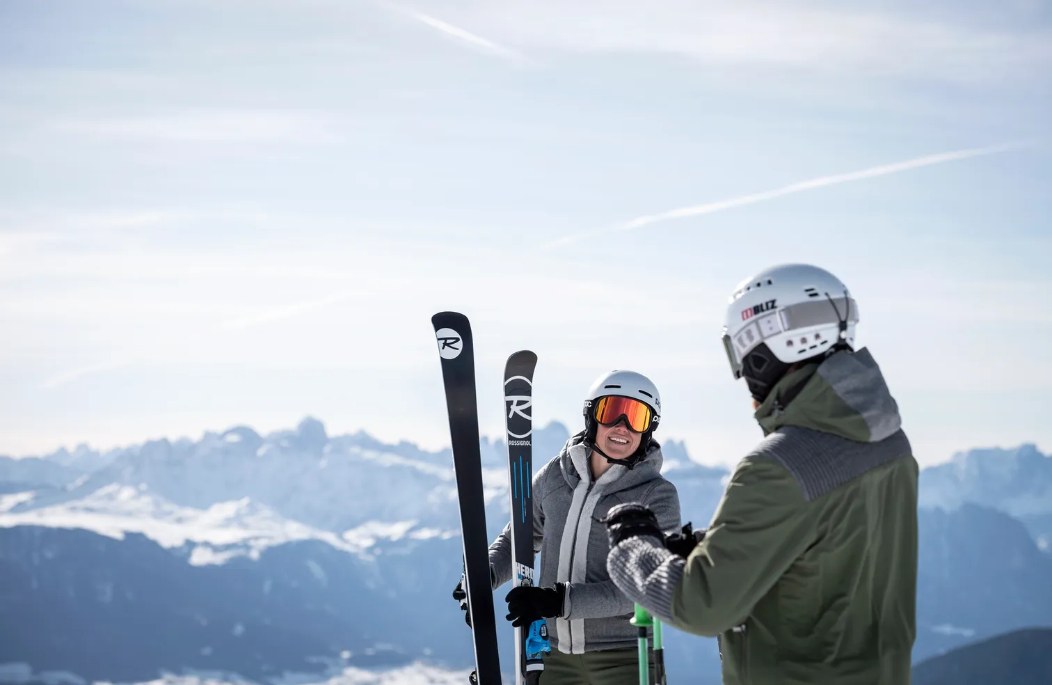 Lächelnde Skifahrerin mit Rossignol-Ski und Begleiter mit Bliz-Helm vor verschneitem Dolomiten-Panorama bei klarem Himmel in Villnöß