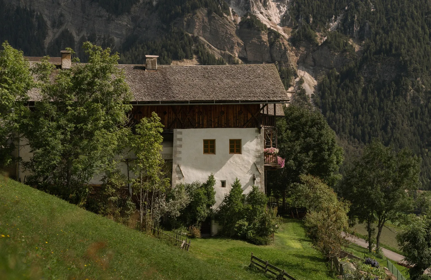 Traditioneller Südtiroler Bauernhof mit Geranien-Balkon vor Bergkulisse im Sommer, Villnöß-Lüsen