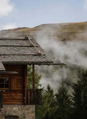Traditional alpine hut with wooden shingle roof and stone base in rising autumn fog in the Dolomite region of Luson