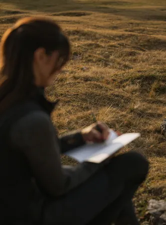 Woman writes in notebook on autumnal alpine meadow in golden evening light in the Geisler Dolomites region Villnöß