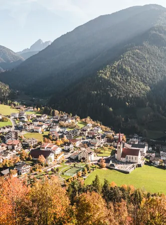 Village of Luson with parish church in colorful autumn dress, sun rays fall into the valley at the foot of the Dolomites, South Tyrol