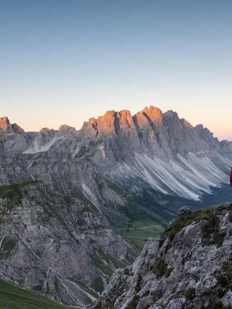 Female climber on the Günther Messner trail with steel cable in rock, Geisler group at sunrise in the background