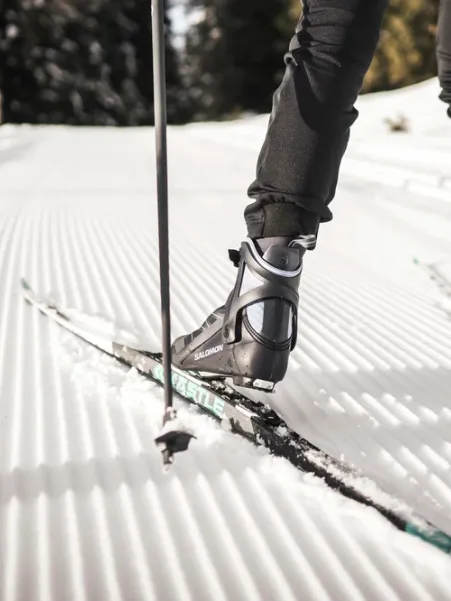 Close-up of cross-country ski boots with Salomon binding on freshly groomed trail in Luson
