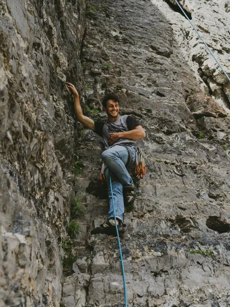 Young climber with harness and quickdraws smiles on rope in steep rock face