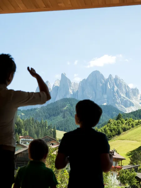 Family with children looks through panoramic window towards Geisler Dolomites and green meadows of Villnöß