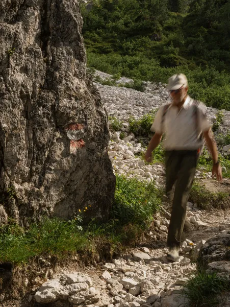 Hiker with cap walks along marked rock path over scree in the Geisler group of the Dolomites in summer