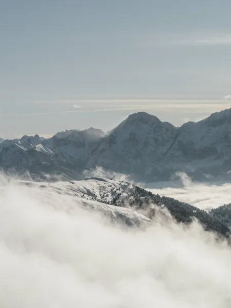 Dolomite peak panorama above dense cloud cover in valley with snow-covered mountain ridges rising from sea of fog in pale winter light above Luson