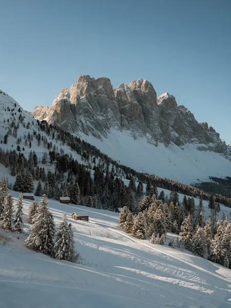 Deeply snow-covered alpine meadows and traditional mountain farms in front of the majestic Peitlerkofel in winter light