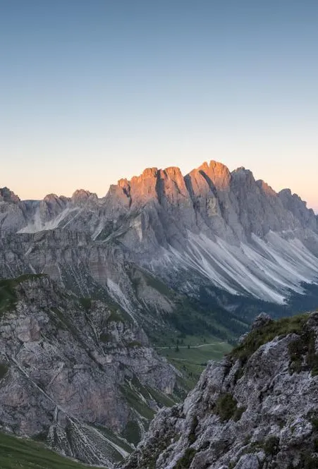 Kletterin am Günther-Messner-Steig mit Stahlseil im Fels, Geislergruppe bei Sonnenaufgang im Hintergrund
