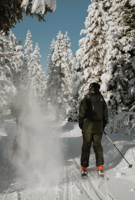 Skitourengeher von hinten auf verschneitem Waldweg mit Pulverschnee von tief verschneiten Fichten bei Sonnenlicht in Lüsen