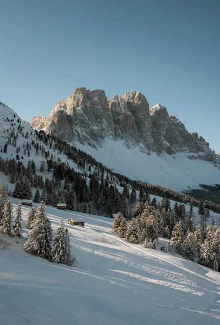 Tief verschneite Almwiesen und traditionelle Bergbauernhöfe vor dem majestätischen Peitlerkofel im Winterlicht