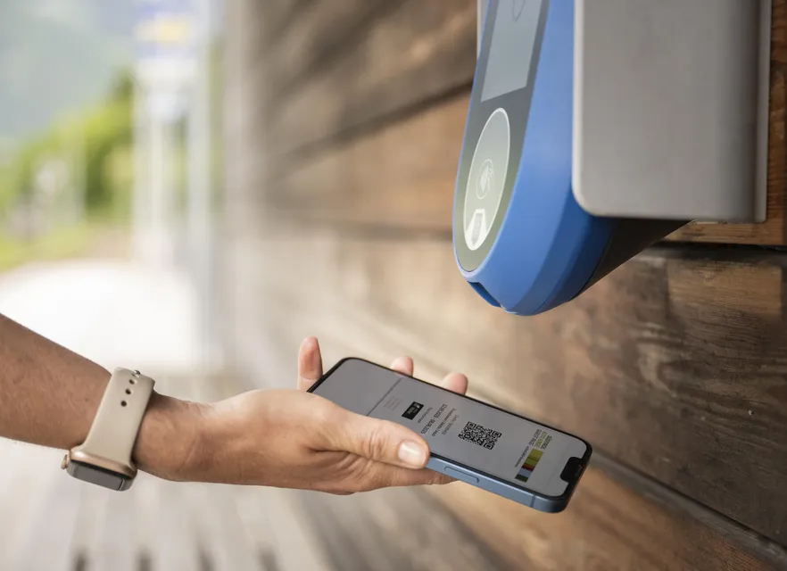 Hand holding smartphone with digital QR code ticket at NFC reader at bus stop – contactless validation in South Tyrol