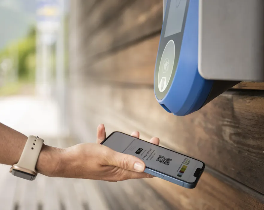 Hand hält Smartphone mit digitalem QR-Code-Ticket an NFC-Lesegerät an Haltestelle – kontaktloses Entwerten in Südtirol